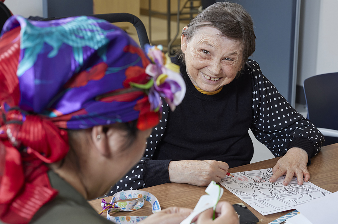 A woman smiling while sitting at a table and speaking with another woman at the table